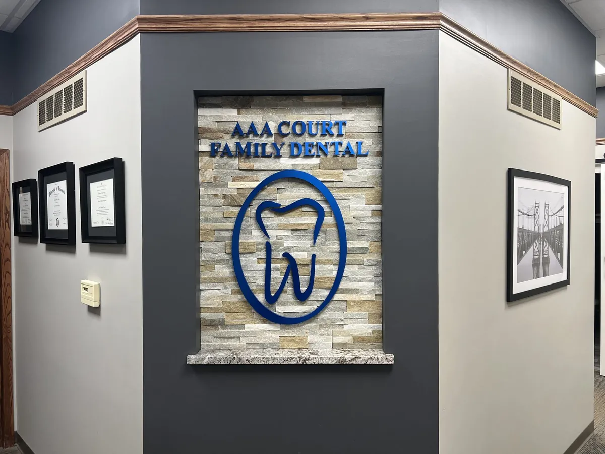 The AAA Court Family Dental interior signature wall, stacked stone, navy raised lettering, the practice's tooth logo, and the doctors' framed diplomas